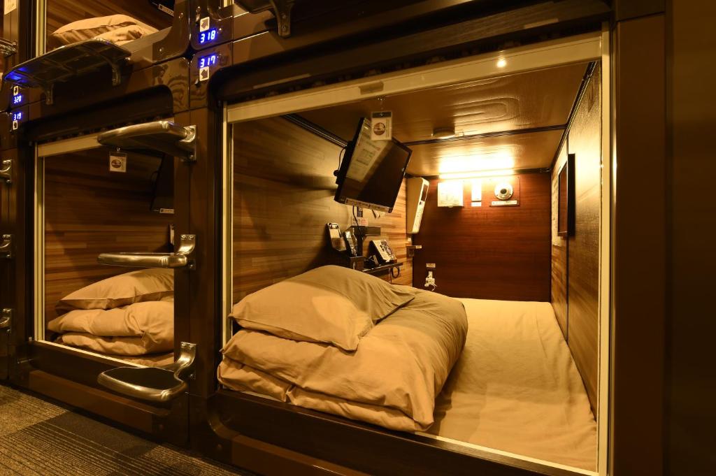 A capsule opening with its blind drawn back in a wall of stacked units - Capsule Hotel Anshin Oyado Shinbashi, Tokyo, Japan